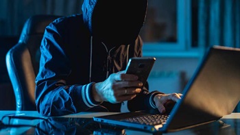 Homem suspeito no computador e com um telemóvel na mão